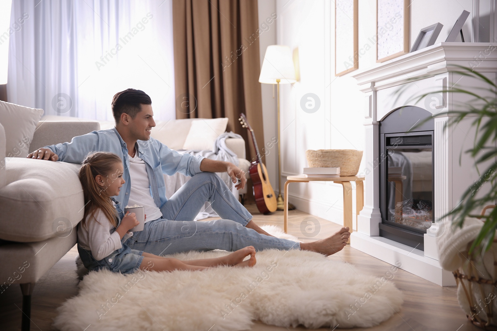 Photo of Happy man with his daughter resting near fireplace at home