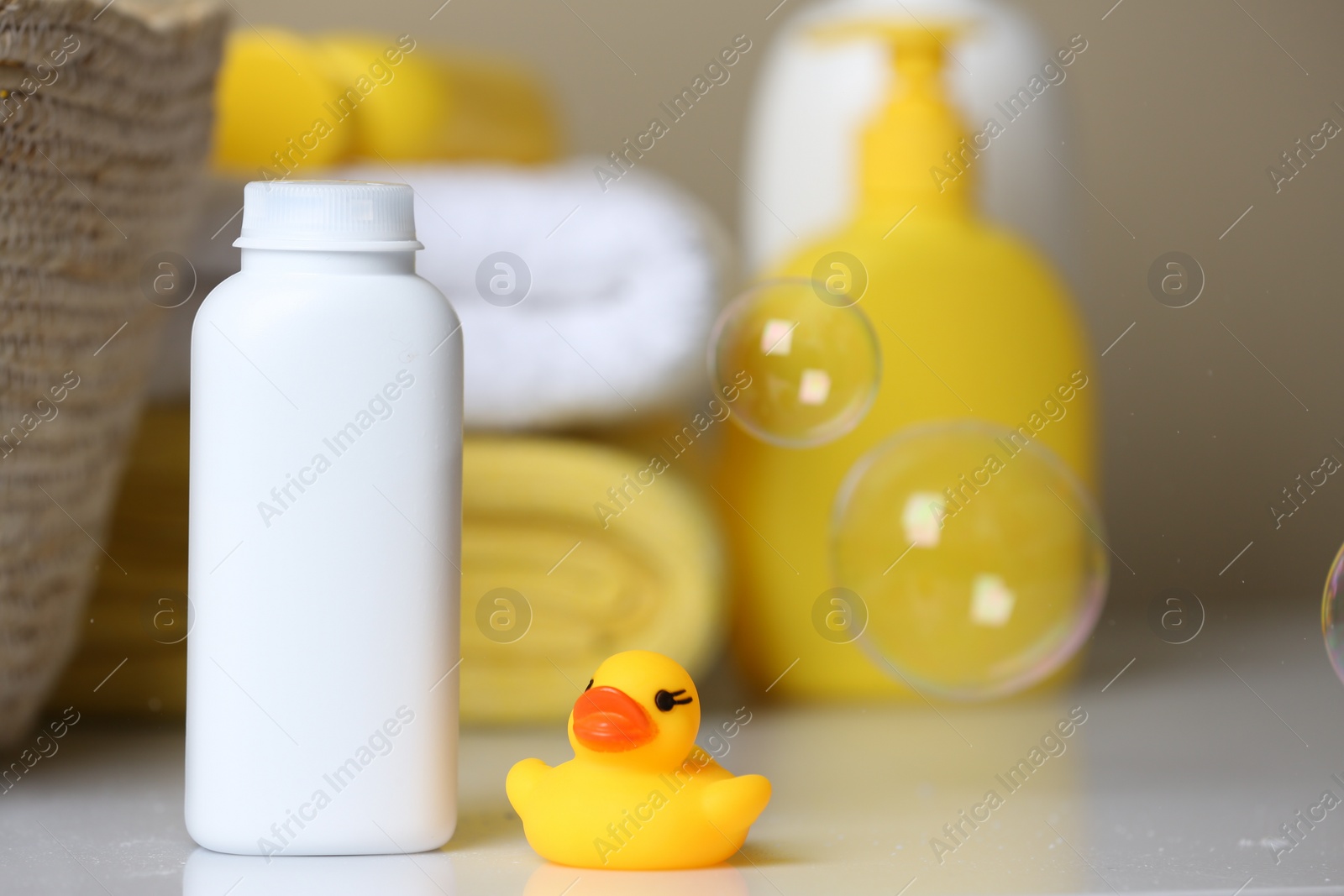 Photo of Bottle of dusting powder and rubber duck on white table, space for text. Baby cosmetic product