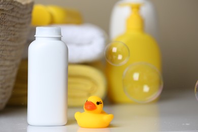 Bottle of dusting powder and rubber duck on white table, space for text. Baby cosmetic product