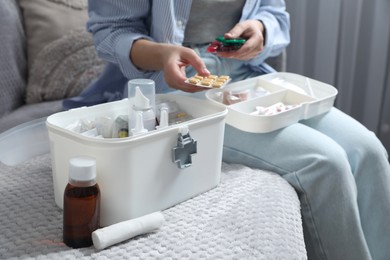 Woman putting pills into first aid kit indoors, closeup