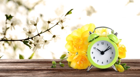 Image of Alarm clock and spring flowers on wooden table, space for text. Time change 