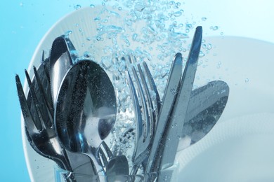 Washing silver cutlery and plates in water on light blue background