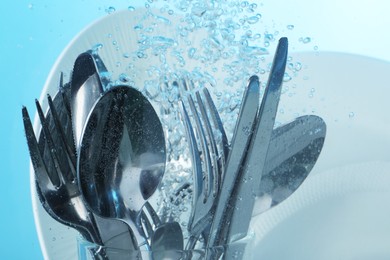 Photo of Washing silver cutlery and plates in water on light blue background