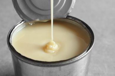 Photo of Condensed milk pouring into tin can on   grey background, closeup. Dairy product