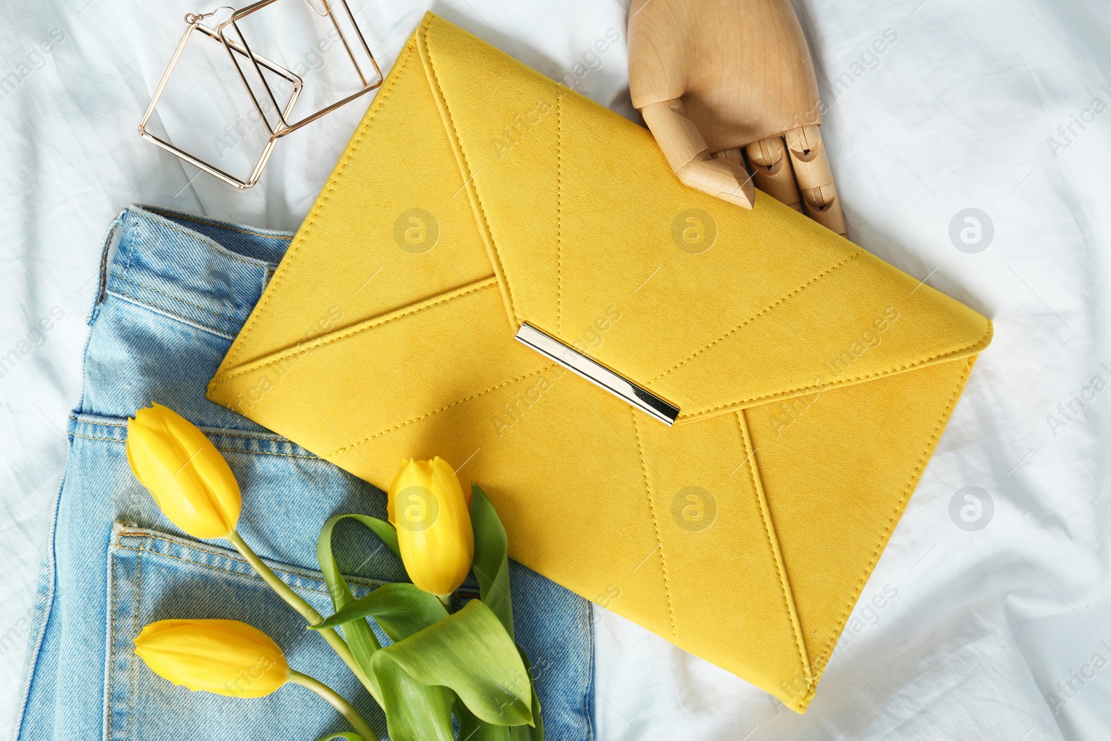 Photo of Composition with stylish envelope bag and flowers on crumpled white sheet, flat lay