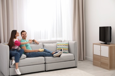 Photo of Couple with snack watching TV on sofa together at home. Space for text