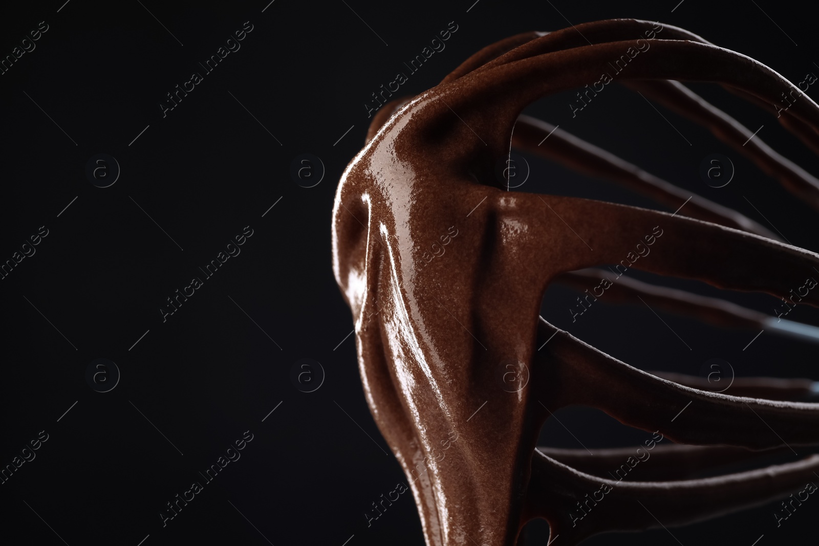 Photo of Chocolate cream flowing from whisk on black background, closeup. Space for text