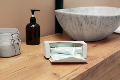 Photo of Package of tampons on wooden countertop in bathroom. Menstrual hygienic product