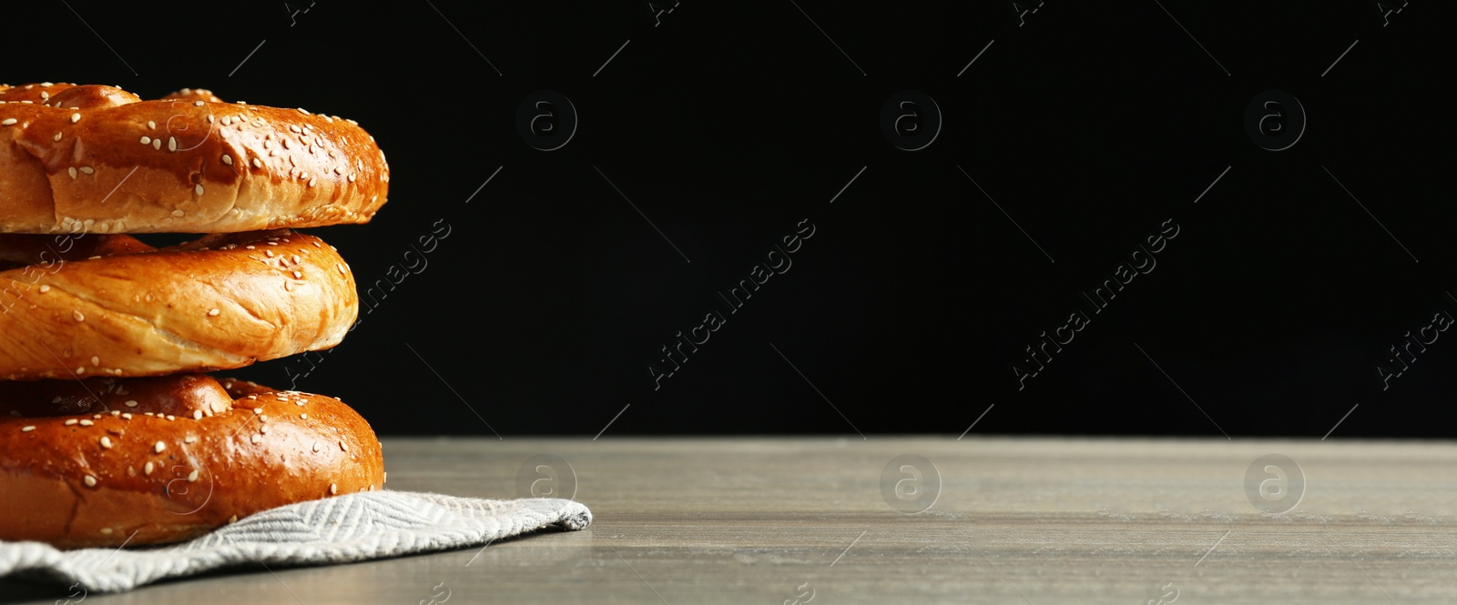 Image of Tasty freshly baked pretzels on wooden table against black background, space for text. Banner design