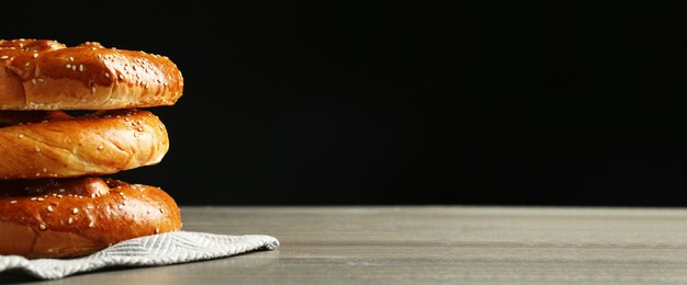 Tasty freshly baked pretzels on wooden table against black background, space for text. Banner design