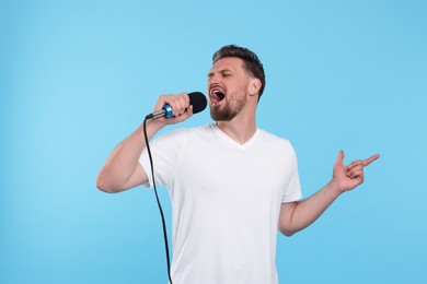 Photo of Handsome man with microphone singing on light blue background