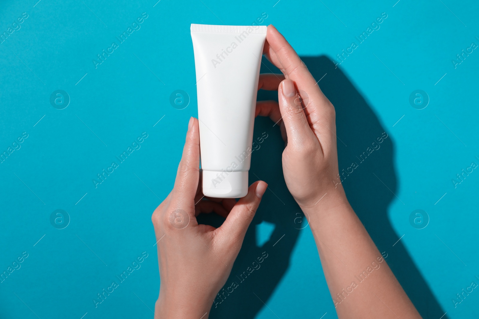 Photo of Woman with tube of hand cream on light blue background, top view