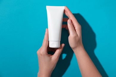 Woman with tube of hand cream on light blue background, top view