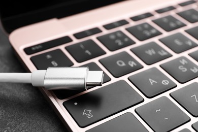 Photo of USB cable with type C connector and laptop on grey table, closeup