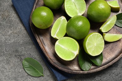 Photo of Fresh ripe limes and leaves on grey table, top view