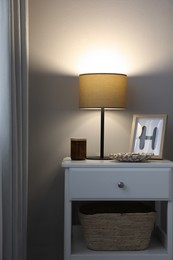 Photo of Stylish lamp and decor on white nightstand in room