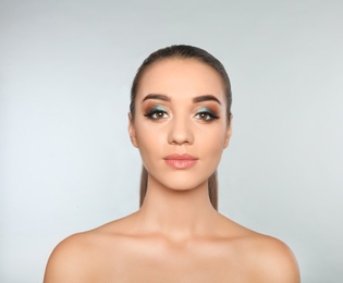 Portrait of young woman with eyelash extensions and beautiful makeup on light background