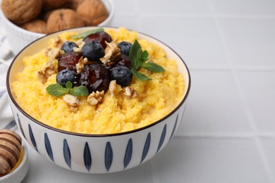 Photo of Tasty cornmeal with blueberries, dates, walnuts and mint in bowl on white table, closeup