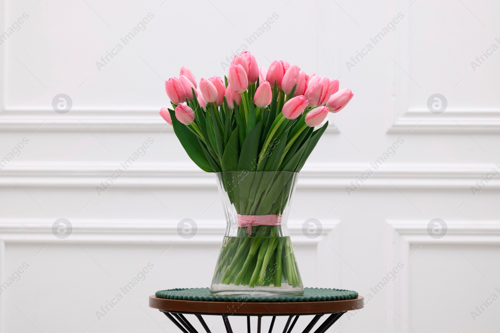 Photo of Bouquet of beautiful pink tulips in vase on table near white wall