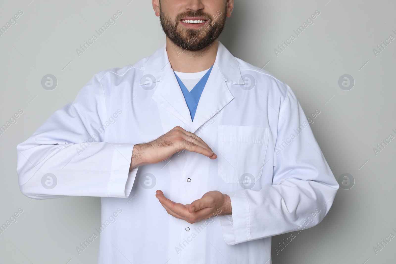 Photo of Young doctor holding something on light grey background, closeup