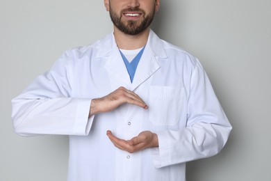 Photo of Young doctor holding something on light grey background, closeup