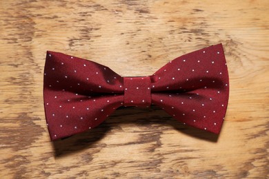 Stylish burgundy bow tie with polka dot pattern on wooden table, top view