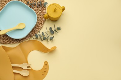 Flat lay composition with baby feeding accessories and bib on yellow background, space for text