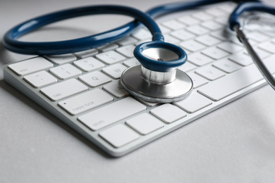 Keyboard and stethoscope on light grey table, closeup. Concept of technical support