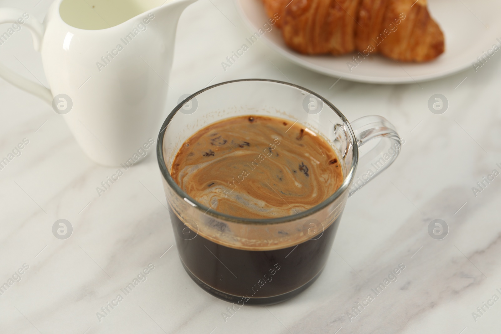 Photo of Aromatic coffee in glass cup and pitcher on white marble table, closeup