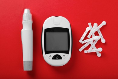 Photo of Digital glucometer, lancets and pen on red background, flat lay. Diabetes control