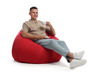 Handsome man drinking coffee on red bean bag chair against white background