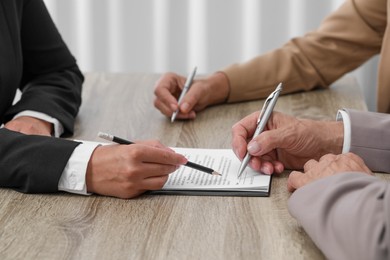 Manager showing client where he must to mark signature at light wooden table indoors, closeup