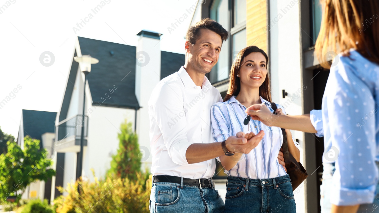 Photo of Real estate agent giving house keys to young couple outdoors