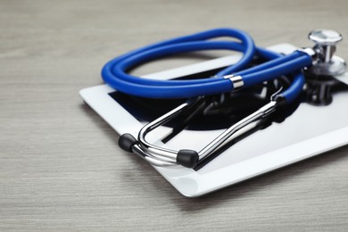 Photo of Computer tablet with stethoscope on wooden table, closeup. Space for text