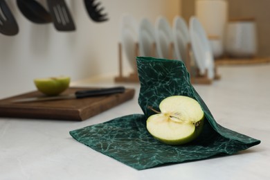 Photo of Half of apple with green beeswax food wrap on white table
