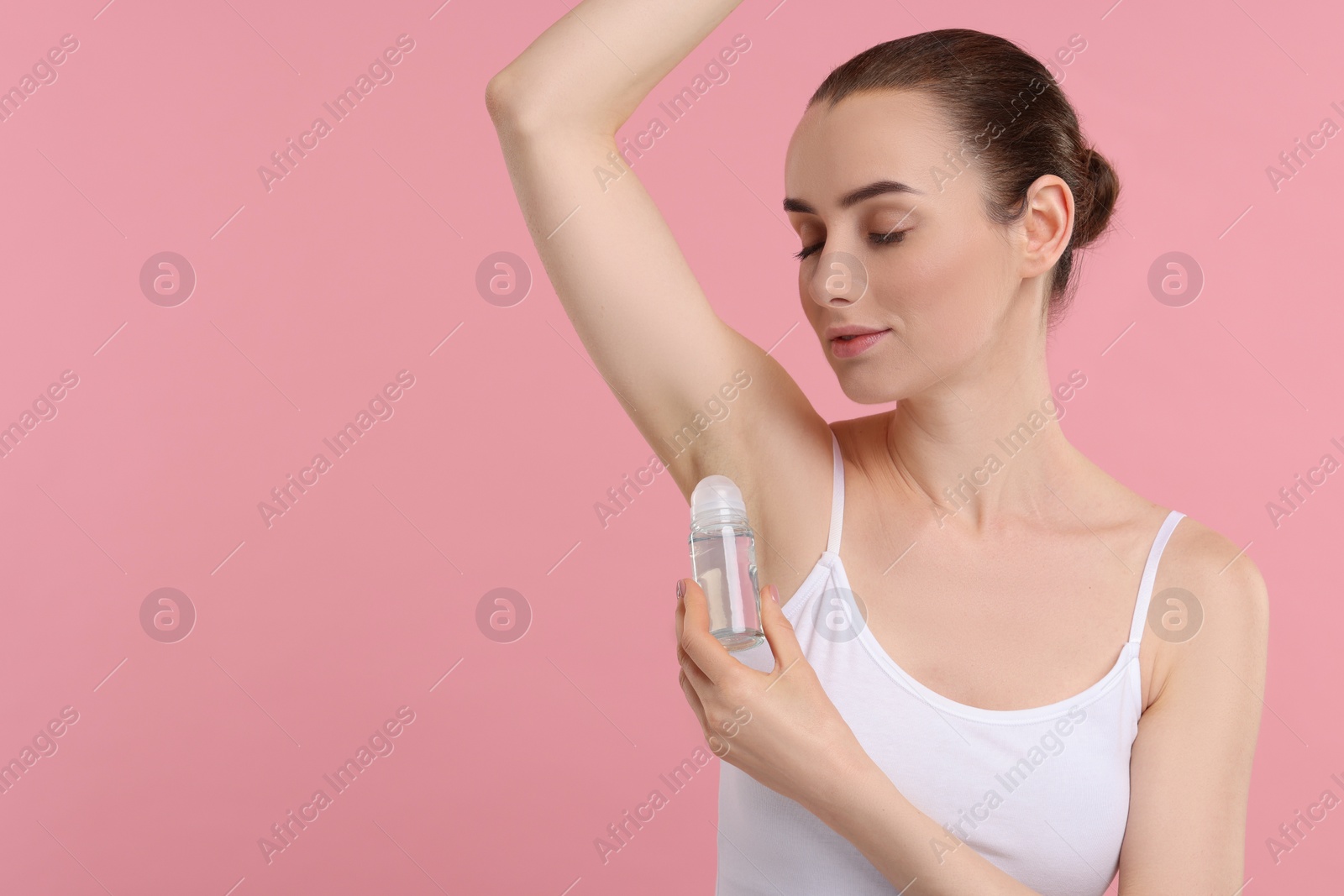 Photo of Beautiful woman applying deodorant on pink background, space for text