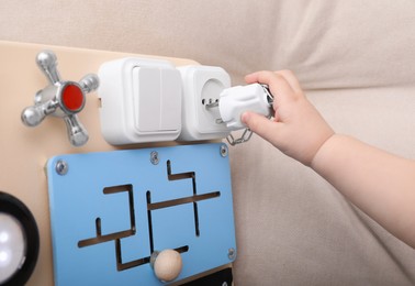 Photo of Little child playing with busy board on sofa, closeup