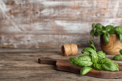 Photo of Board with fresh basil leaves on wooden table. Space for text