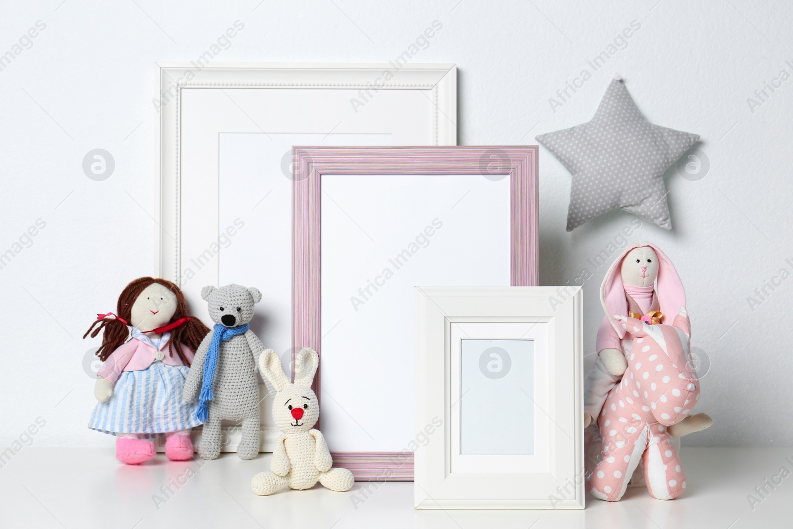 Photo of Soft toys and photo frames on table against white background, space for text. Child room interior