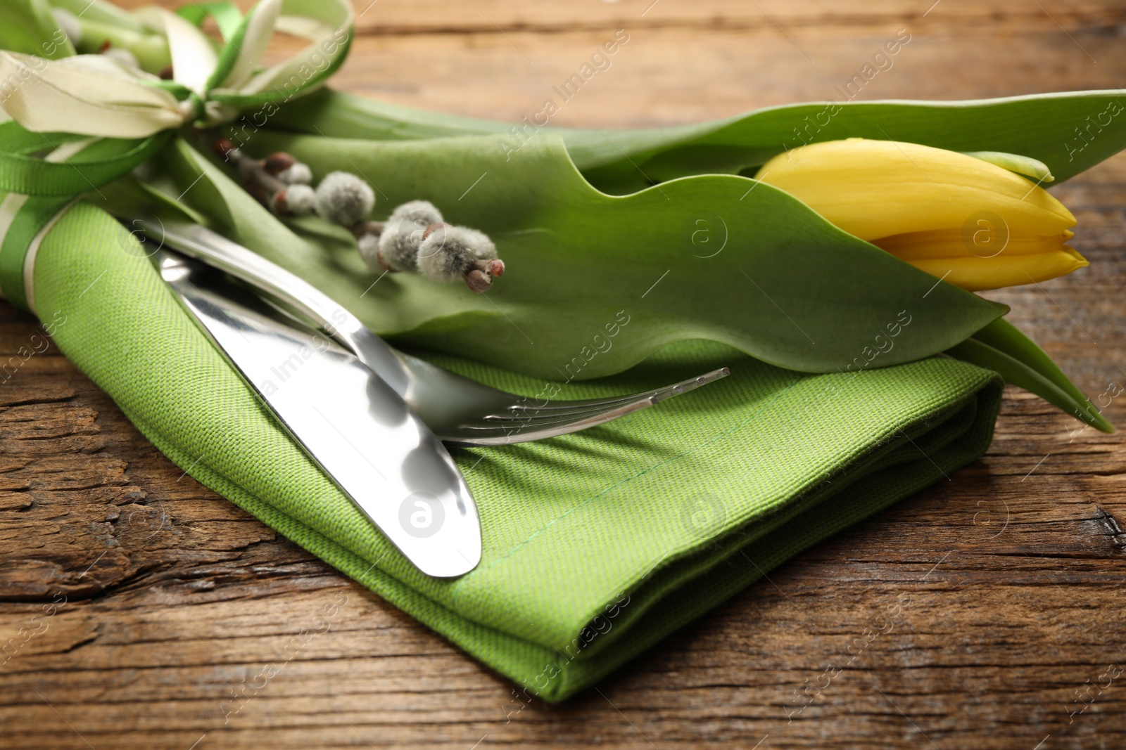 Photo of Cutlery set with beautiful willow branch and tulip on wooden table, closeup. Easter celebration