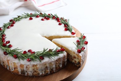 Photo of Traditional Christmas cake decorated with rosemary and pomegranate seeds on white table, closeup