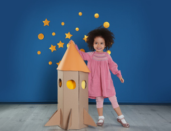 Photo of Cute African American child playing with cardboard rocket near blue wall