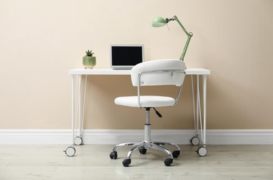 Stylish workplace with laptop and comfortable chair near beige wall indoors. Interior design
