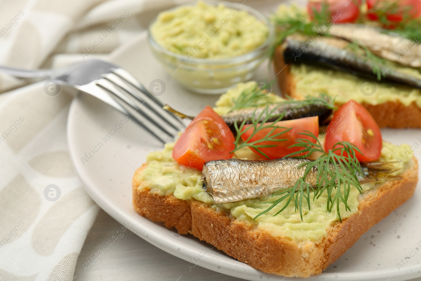 Delicious sandwiches with sprats, tomatoes, dill and avocado puree served on white table, closeup Photo of Delicious sandwiches with sprats, tomatoes, dill and avocado puree served on white table, closeup