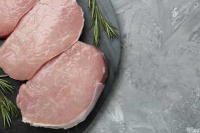 Photo of Pieces of raw pork meat and rosemary on grey textured table, top view. Space for text