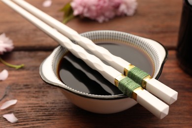 Photo of Bowl with soy sauce and chopsticks on wooden table, closeup