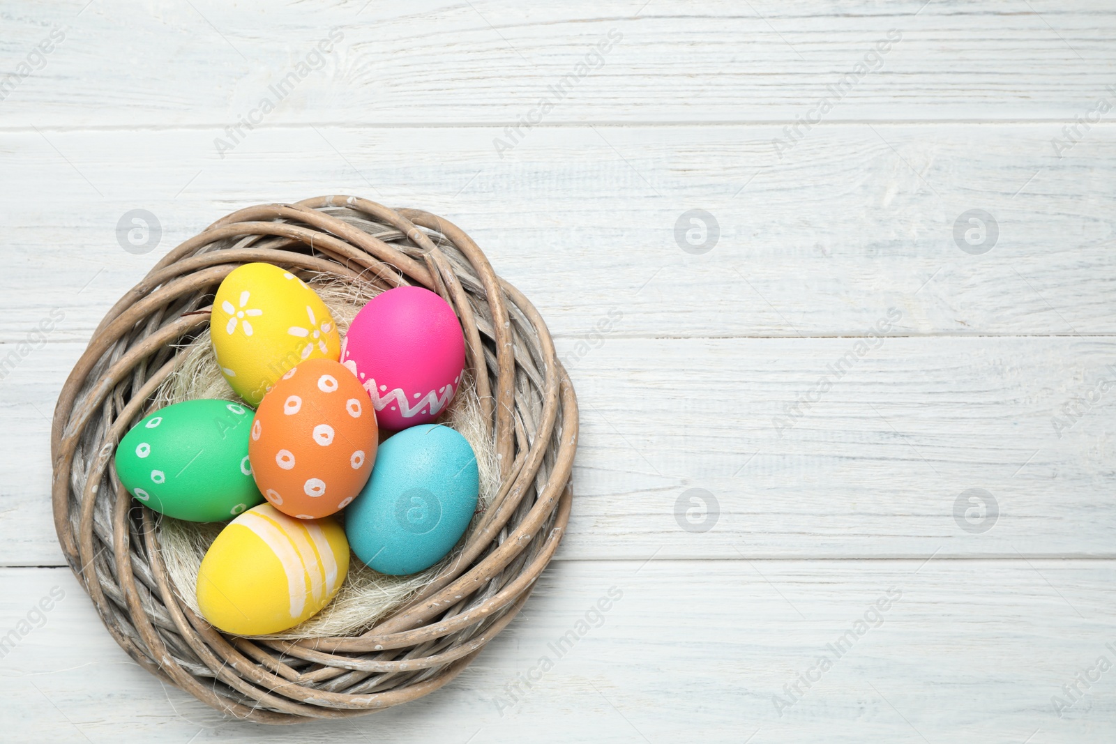 Photo of Decorative nest with Easter eggs on white wooden background, top view. Space for text
