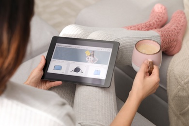 Woman with cup of coffee using tablet for online shopping indoors, closeup
