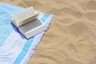 Beach towel with open book on sand, space for text