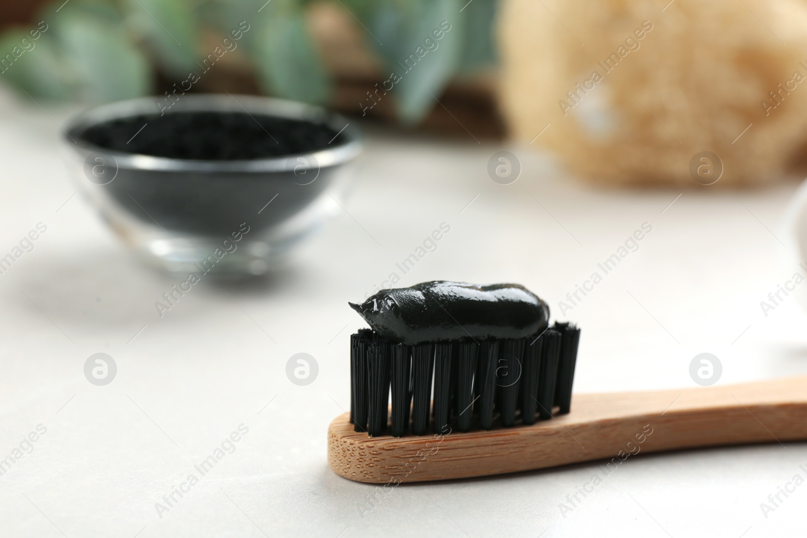 Photo of Bamboo toothbrush with charcoal paste on white table, closeup. Space for text